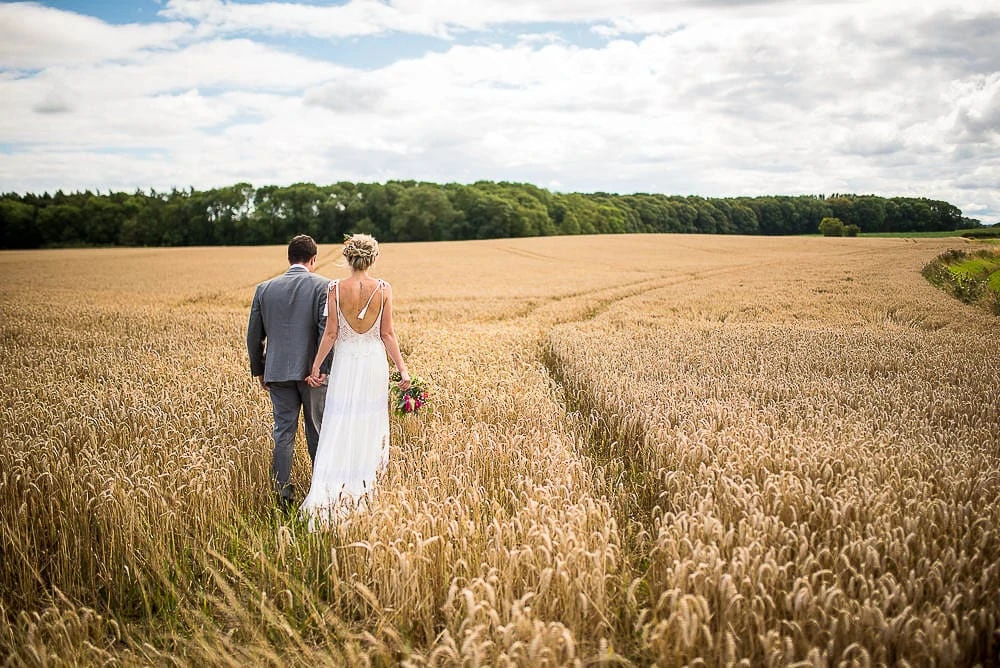 bride and groom walking in corn fields at priory cottages