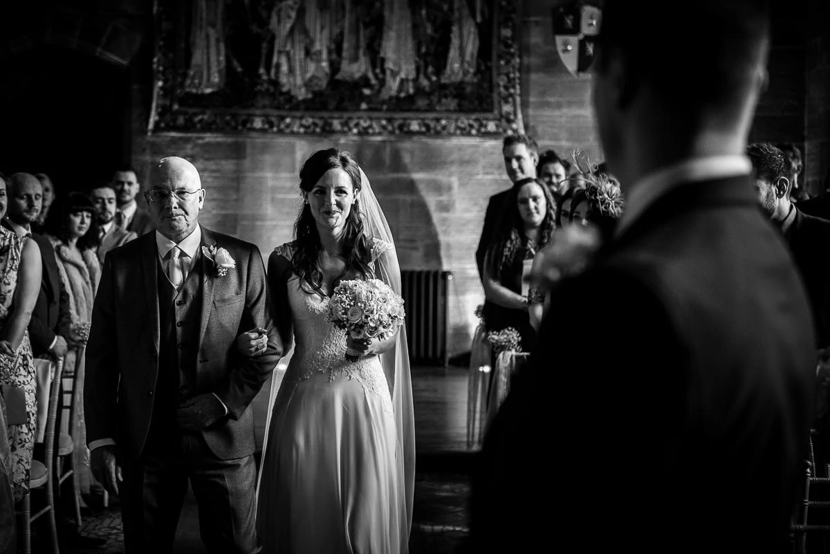black and white photo of bride walking up the aisle at peckforton castle