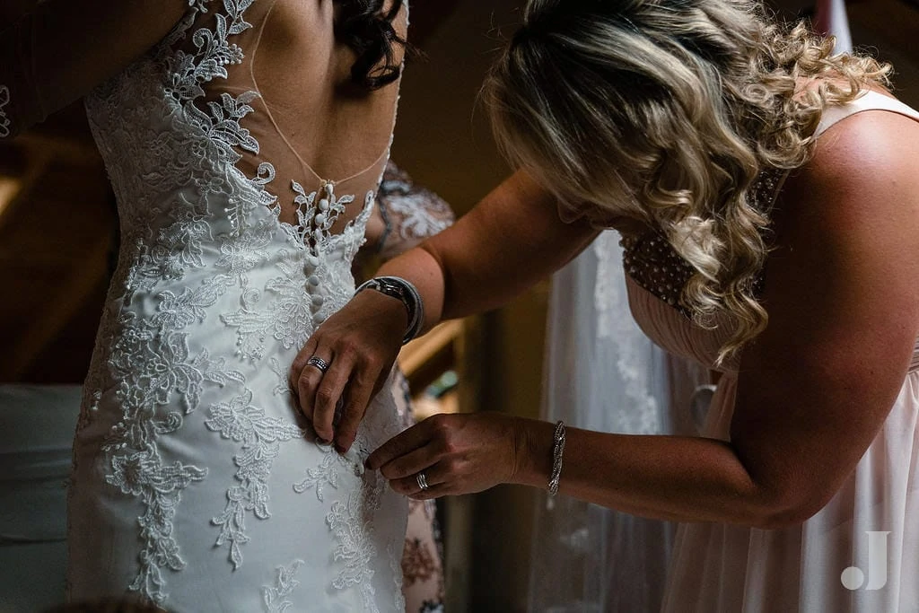 bride being buttoned in to her dress at oak tree of peover